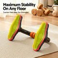 Underside of push-up stand showing yellow-green non-slip traction pads on rug with dumbbells in background