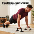 Man in red t-shirt doing push-ups on black push-up stands on rug in home gym with dumbbells and kettlebell