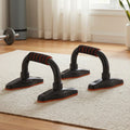 Two black push-up stands on cream rug in home gym beside barbell, three-quarter view