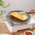 Omelette being flipped on a non-stick pan with tongs, placed on a portable stove.