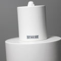 Close-up of white cylindrical spotlight head with E27 MAX. 60W label sticker, pivot joint at top, grey background