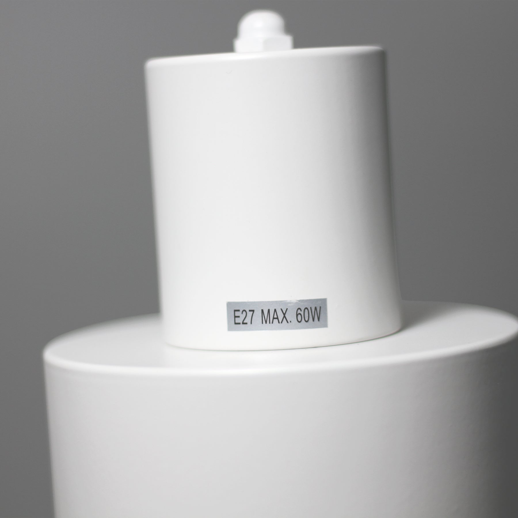 Close-up of white cylindrical spotlight head with E27 MAX. 60W label sticker, pivot joint at top, grey background