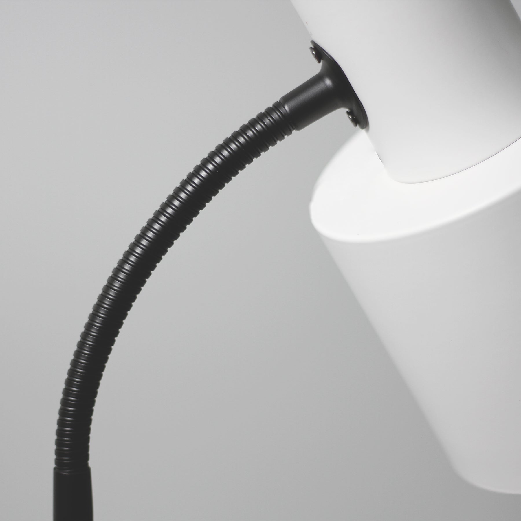 Close-up of black ribbed flexible gooseneck connecting to white cylindrical spotlight head on grey background