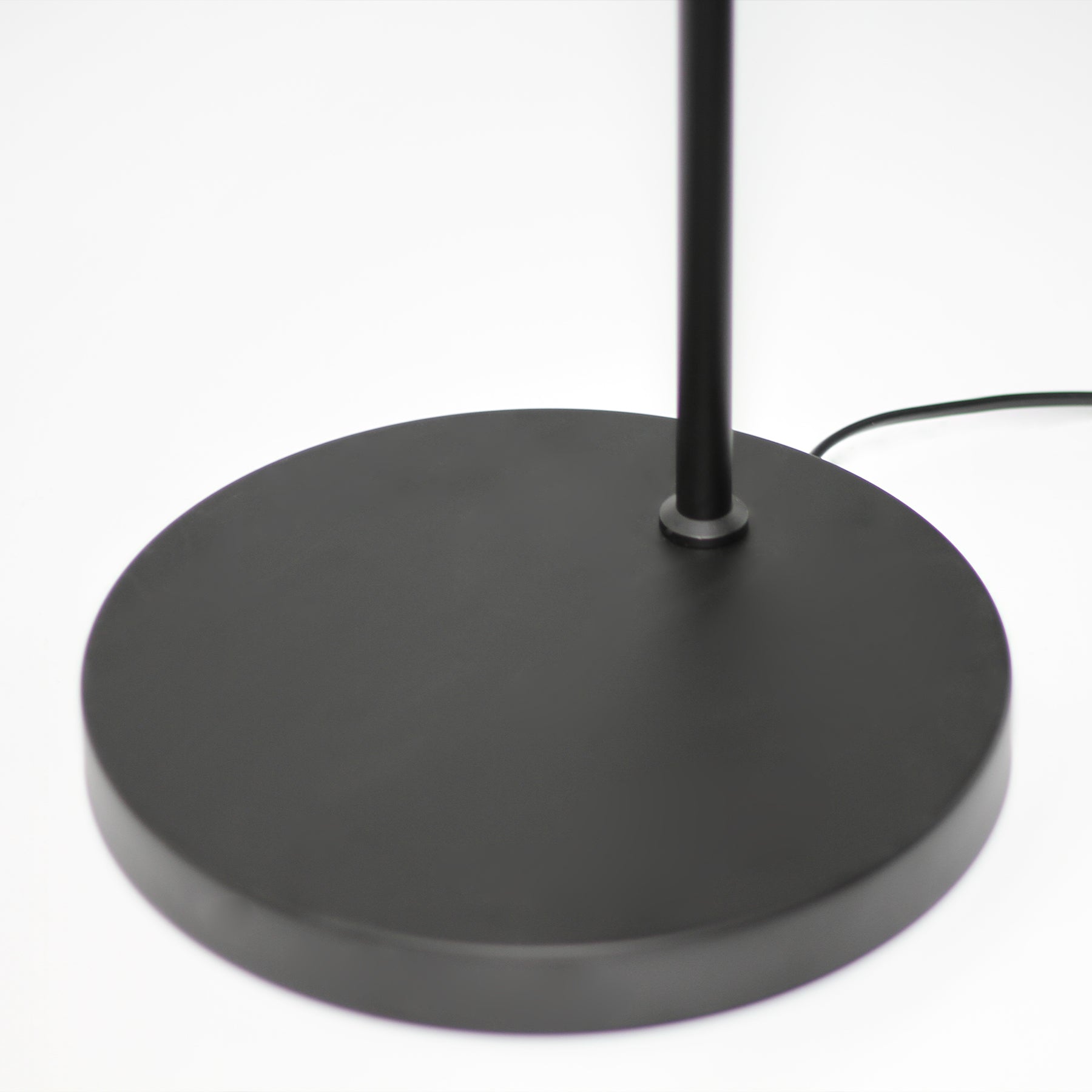 Close-up of flat round black metal base of arc reading lamp with thin pole and black power cord on white background