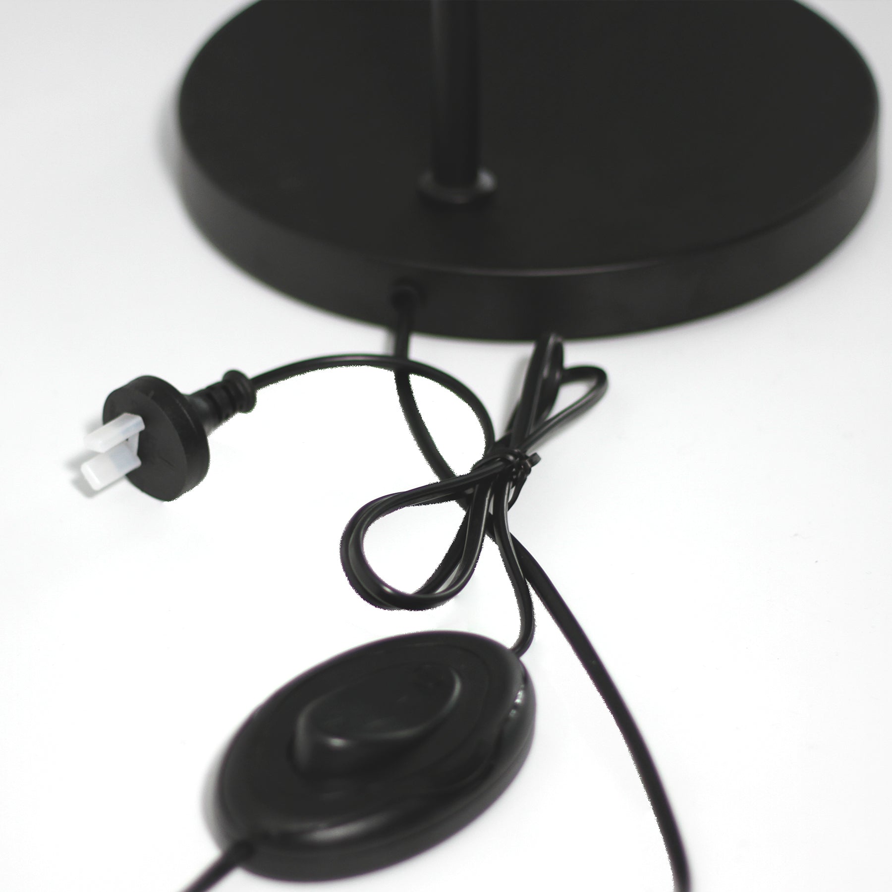 Close-up of arc reading lamp base showing black cord, Australian power plug and oval foot switch on white background