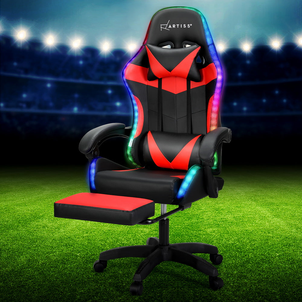 Artiss black and red LED massage gaming chair in stadium setting on grass with footrest extended and RGB lit