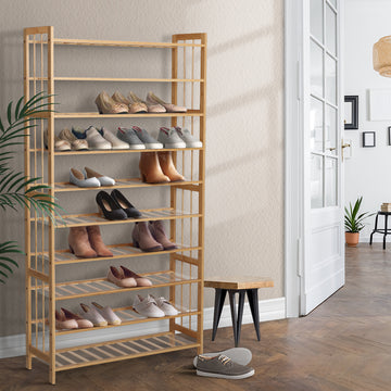 Natural bamboo 9-tier shoe rack loaded with shoes in hallway with French doors plant and small stool