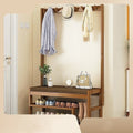 Bamboo coat rack in entryway with coats and hat on hooks, shoes on lower shelves, bag and plant on bench shelf