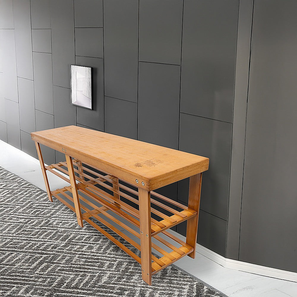 Natural bamboo shoe bench in styled hallway with dark grey wall tiles, geometric rug underfoot