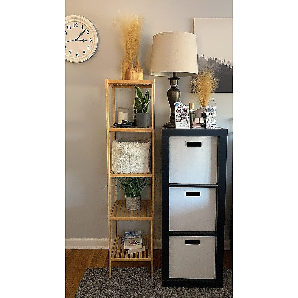 Bamboo slim shelving unit in bedroom styled with plants, white cushion and books beside a wall clock and table lamp