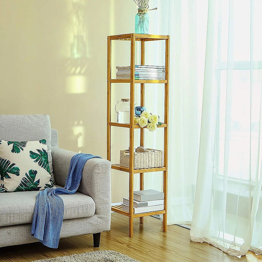 Bamboo slim shelving unit in bright living room with books, roses and wicker basket beside grey sofa and white curtains