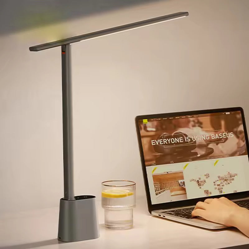 Baseus grey slim LED desk lamp with T-bar head on desk beside open laptop and glass of lemon water