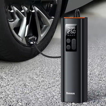 Baseus portable tyre inflator connected to car tyre on asphalt, LCD display showing PSI BAR 2.60, orange cap, control buttons