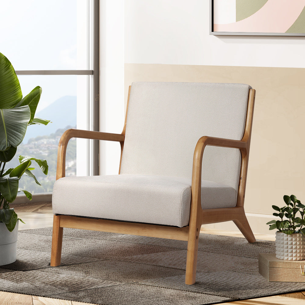 Beige fabric armchair with curved wood frame and open armrests in lifestyle room scene with large tropical plant