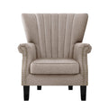 Beige fabric channel-stitched wingback armchair with gold nailhead trim on arms, black legs, front view on white background