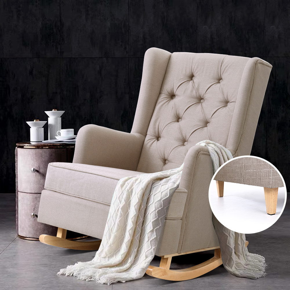 Beige fabric tufted wingback rocking chair with white throw beside pink vintage nightstand, dark stone wall background