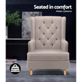 Beige linen fabric tufted wingback chair front view in dark room with plant, 150KG max load badge, text: Seated in comfort