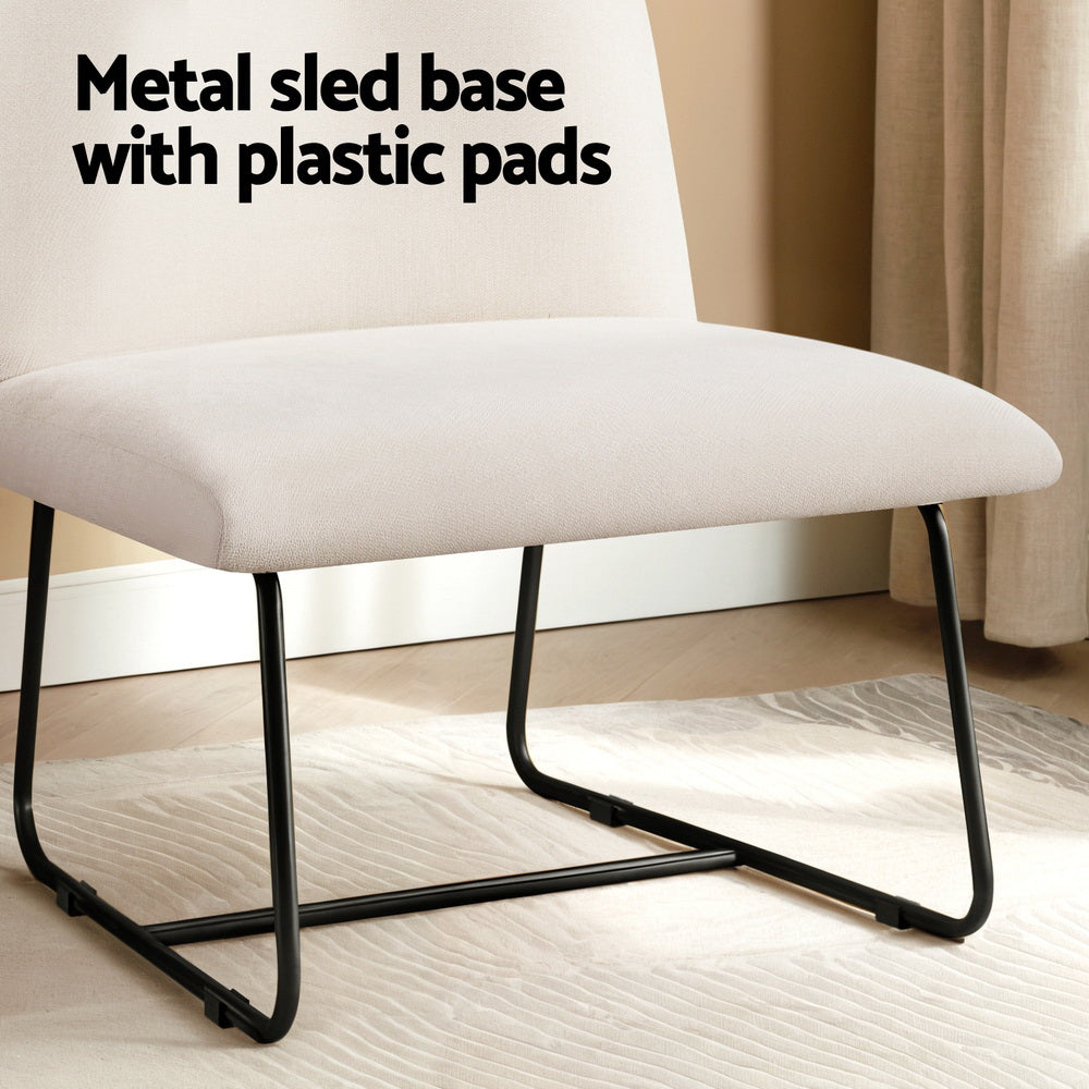 Beige linen accent chair seat close-up with black metal sled base and plastic floor pads, in room with rug and curtains