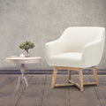 Beige linen barrel armchair beside round dark wood side table with pampas grass, white wall and wood floor setting