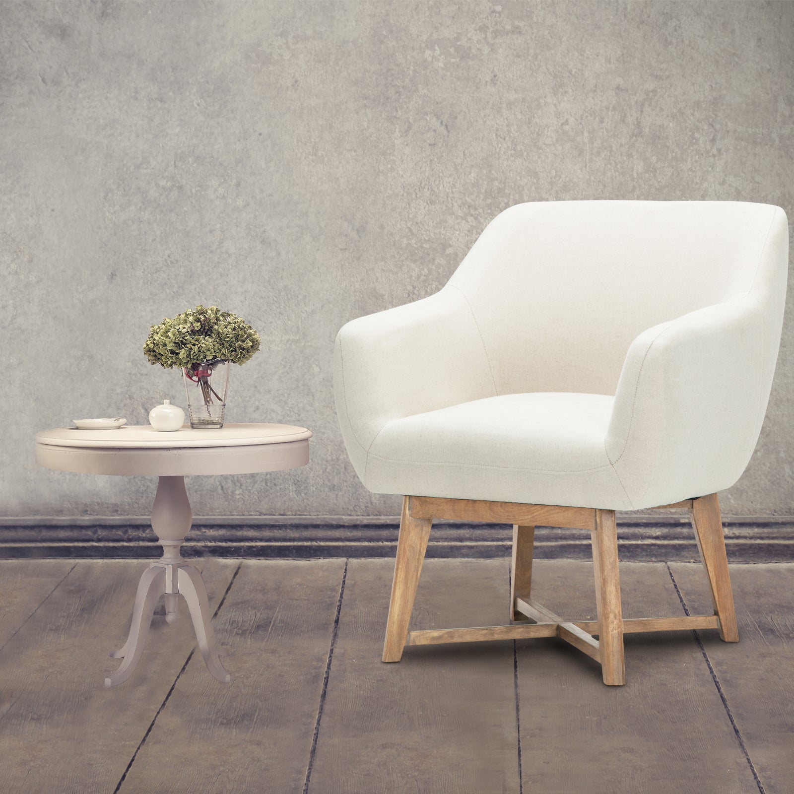 Beige linen barrel armchair beside round dark wood side table with pampas grass, white wall and wood floor setting
