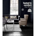 Beige nailhead wingback armchair in dark living room with dark sofa and white coffee table, 150KG max load badge