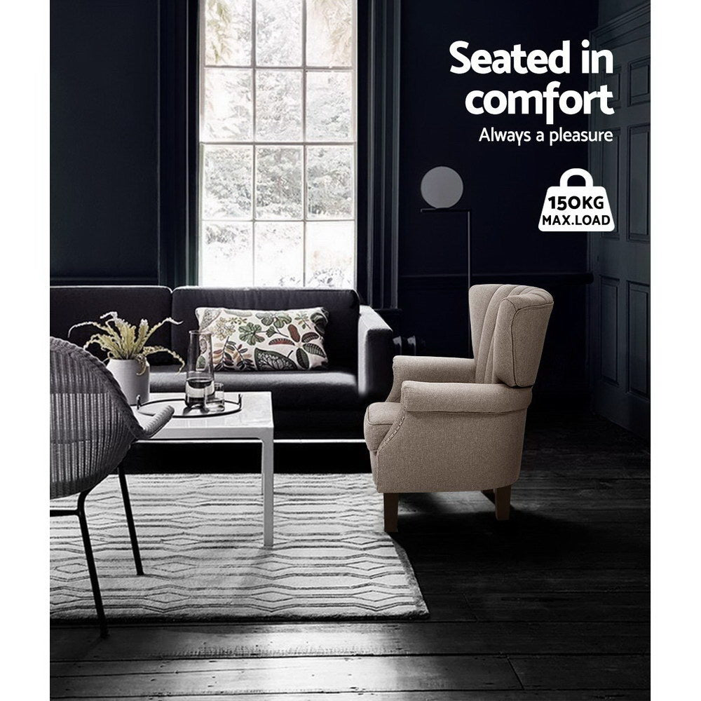 Beige nailhead wingback armchair in dark living room with dark sofa and white coffee table, 150KG max load badge