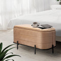 Beige velvet storage bench with horizontal channel tufting and black metal legs, topped with a wood tray holding a cup and