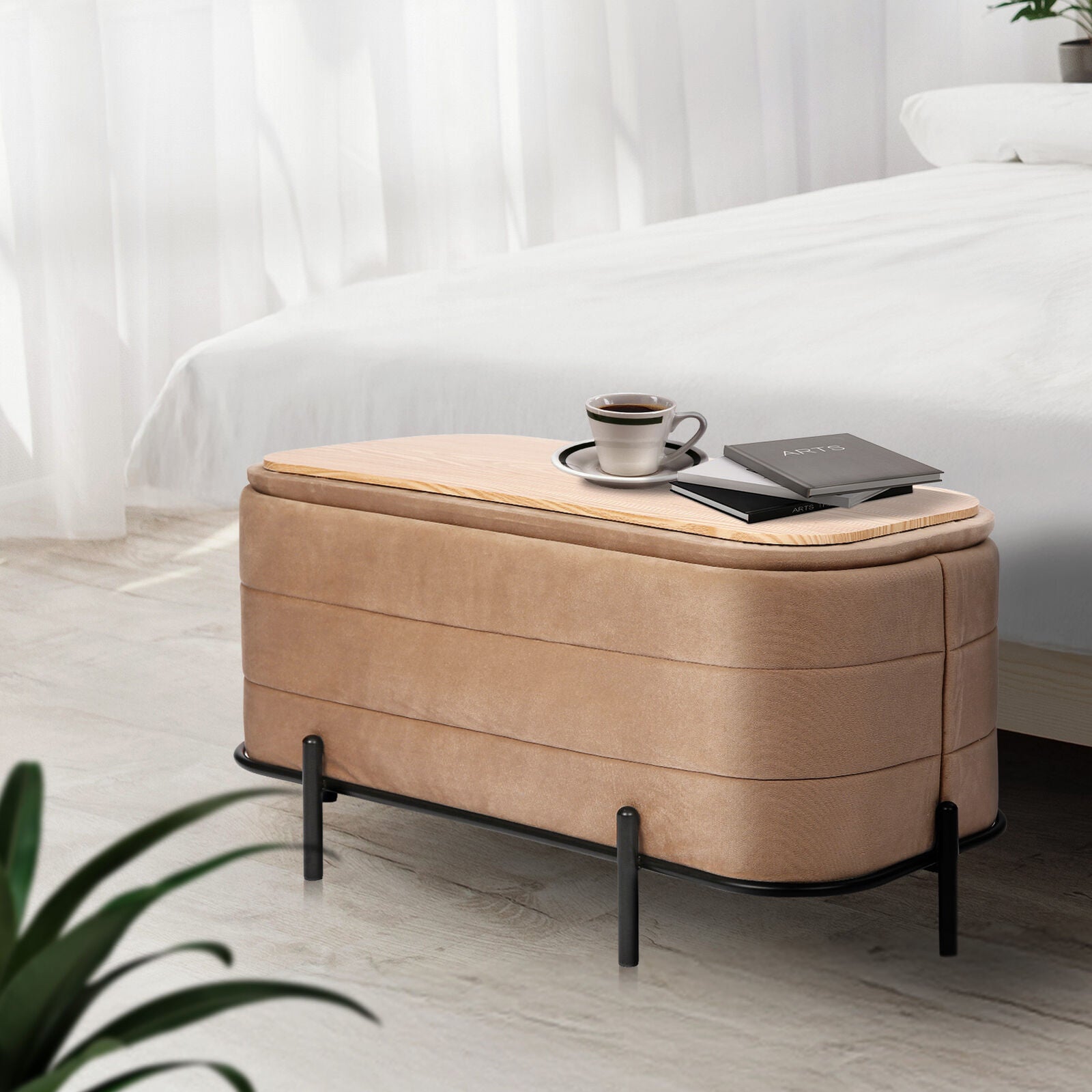 Beige velvet storage bench with horizontal channel tufting and black metal legs, topped with a wood tray holding a cup and