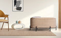 Beige velvet rectangular storage bench on black metal frame placed on a rug in a living room beside a yellow armchair and
