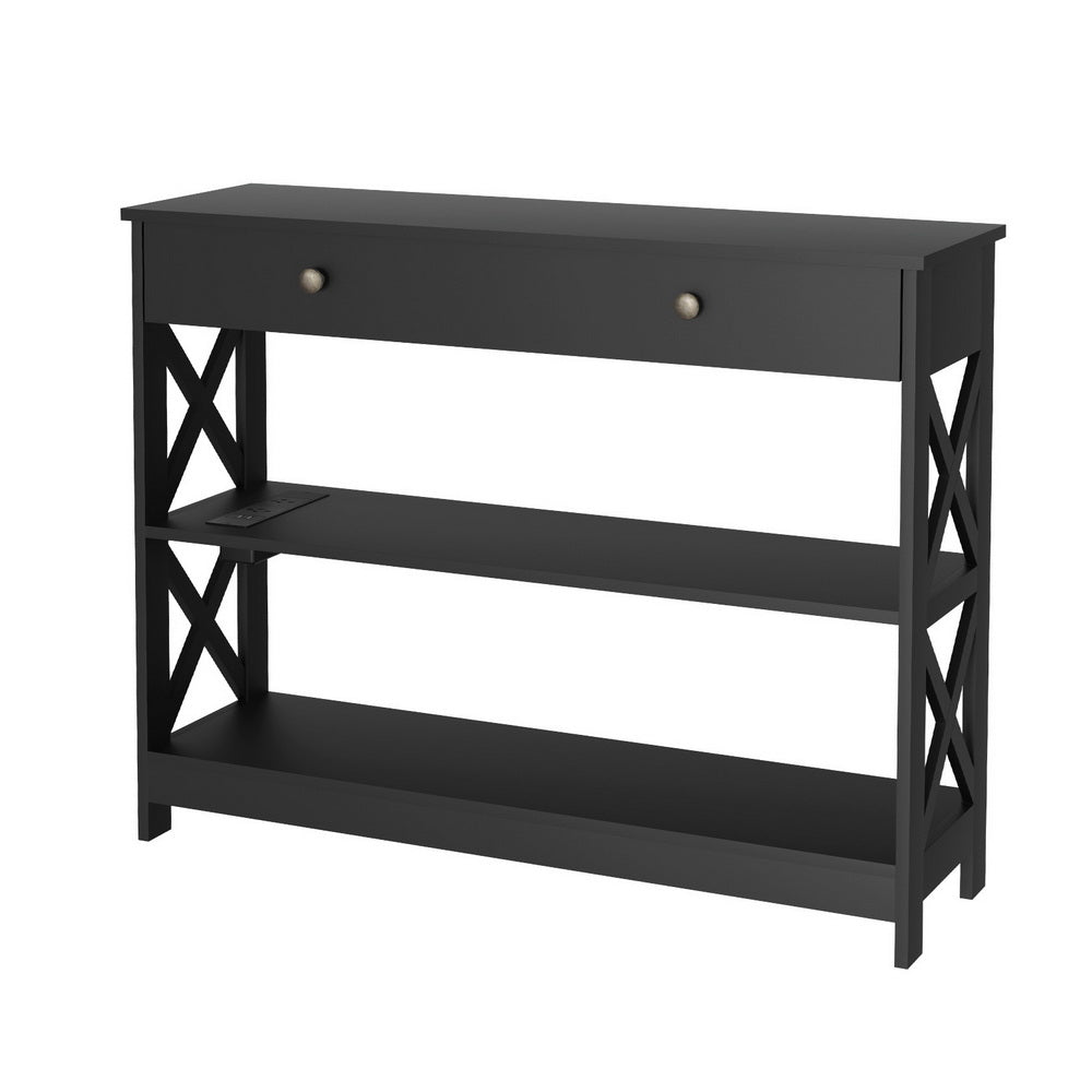 Black console table with one drawer, X-cross panels, two lower shelves and built-in power outlet, angle view on white