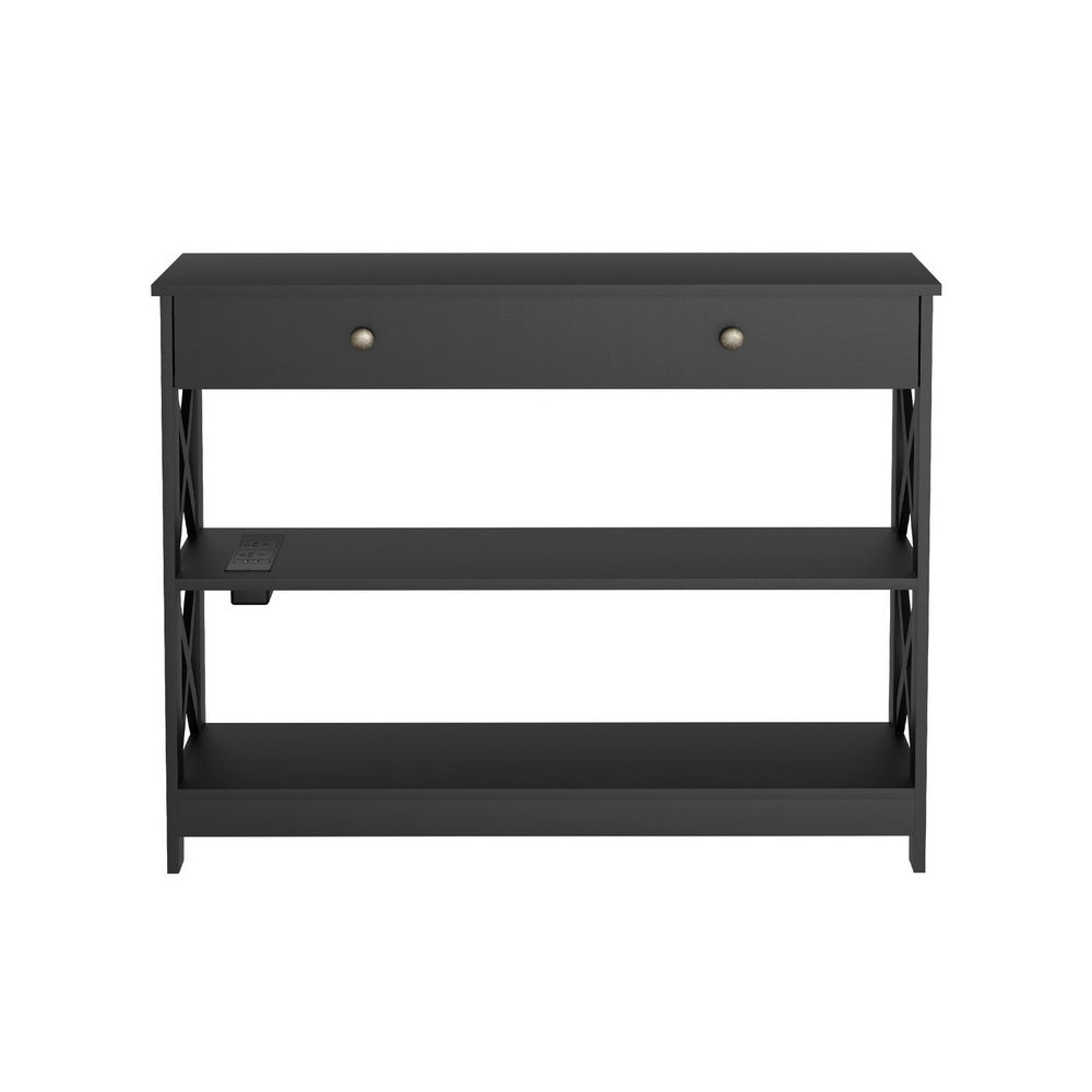 Black console table front view, one drawer, X-cross panels, two lower shelves and power outlet on middle shelf
