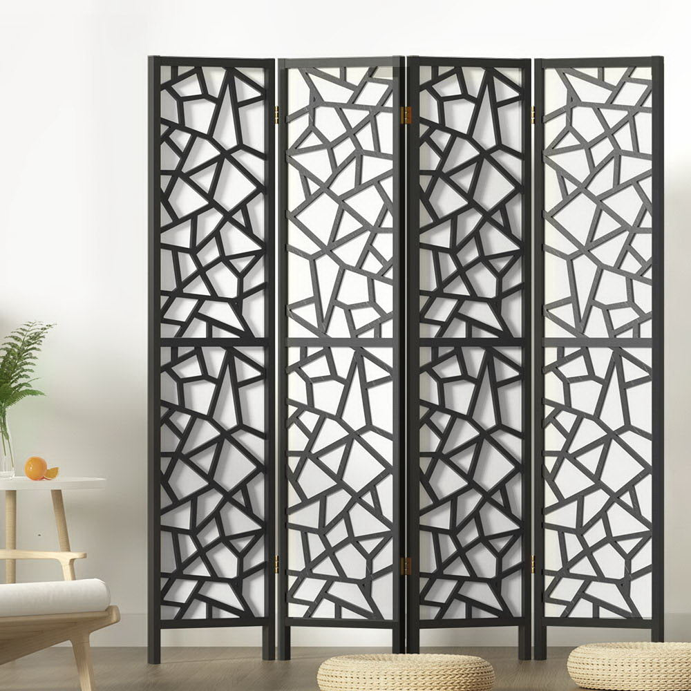 Black 4-panel criss-cross geometric cutout room divider in lifestyle room with fern plant and floor cushions