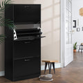 Black four-tier flip-out shoe cabinet second compartment tray open in hallway lifestyle with wooden stool and palm plant
