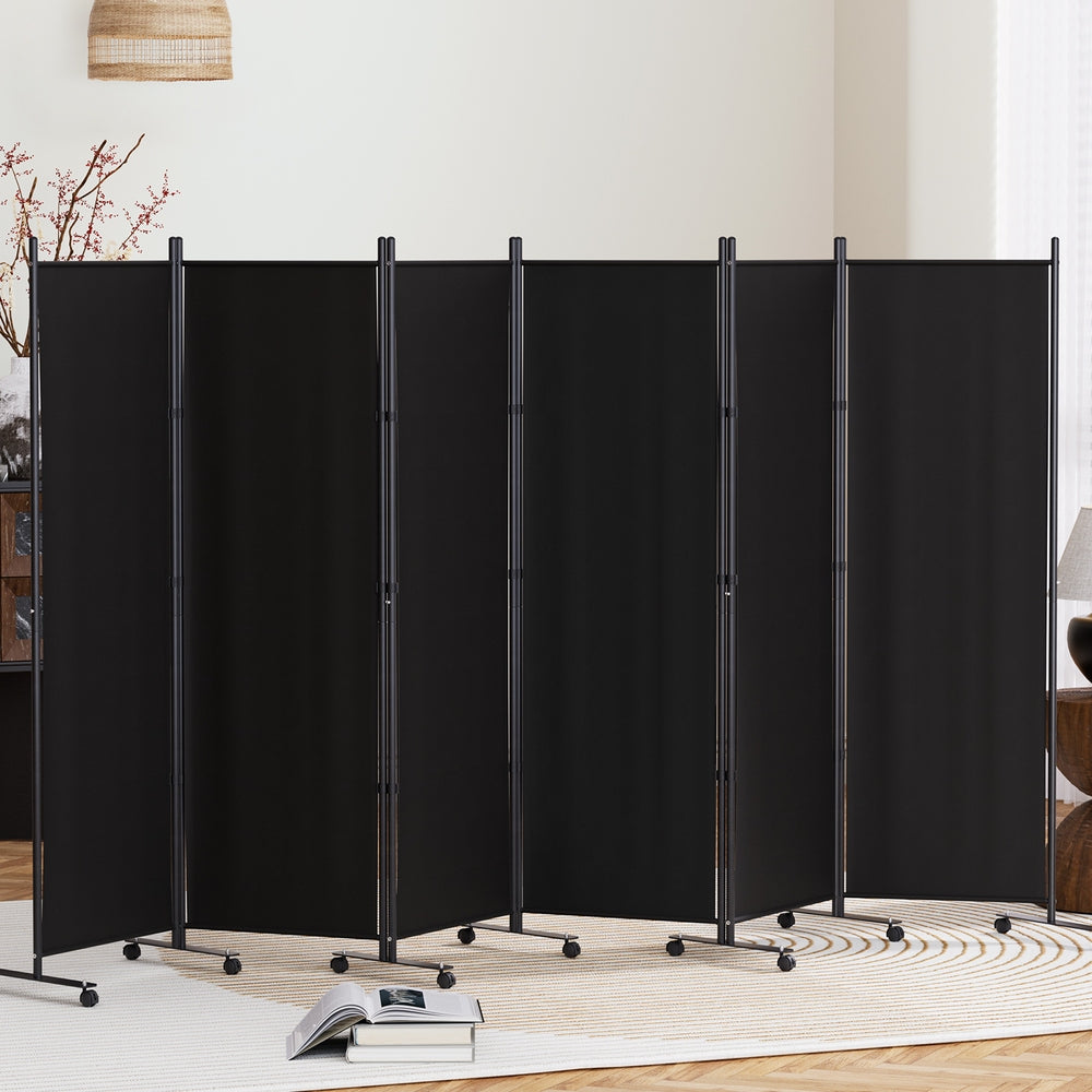 Black 6-panel fabric room divider on wheels in living room lifestyle with red berry branch vase and open books on rug
