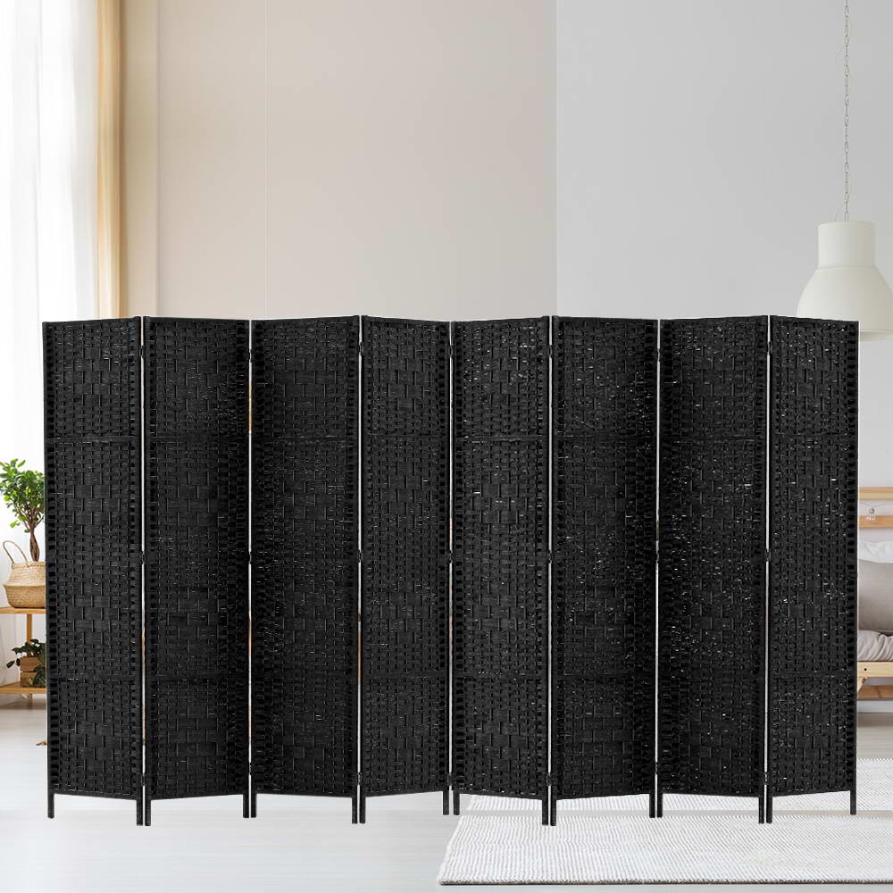 Black 8-panel woven paper rope room divider in lifestyle room against white wall with hanging plant and rattan pendant lamp