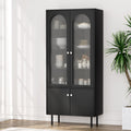 Tall black cabinet with two arched fluted glass upper doors and two solid lower doors, dinnerware visible inside, metal legs