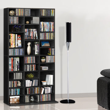 Black multi-column CD and DVD media storage shelf loaded with discs in living room beside floor speaker