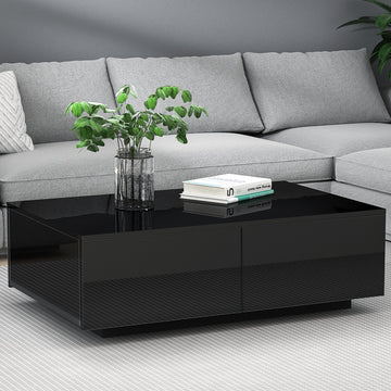 Black high-gloss rectangular coffee table with four drawers and textured panel front, styled with a plant and books in a