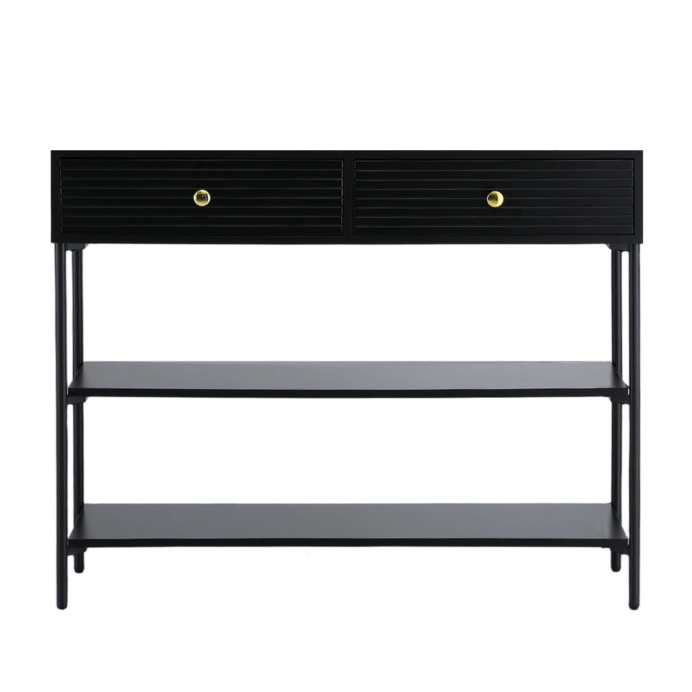 Black console table with two ribbed drawers with gold knobs, two open lower shelves, and thin metal legs, angle view