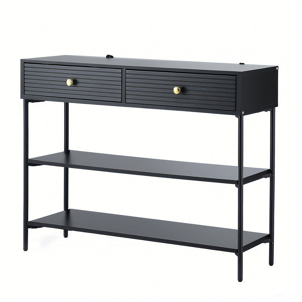 Black console table with two ribbed drawers with gold knobs, two open lower shelves, and thin metal legs, angle view