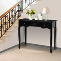 Black wooden console table with three drawers and ornate cabriole legs styled with flowers and lamp by staircase