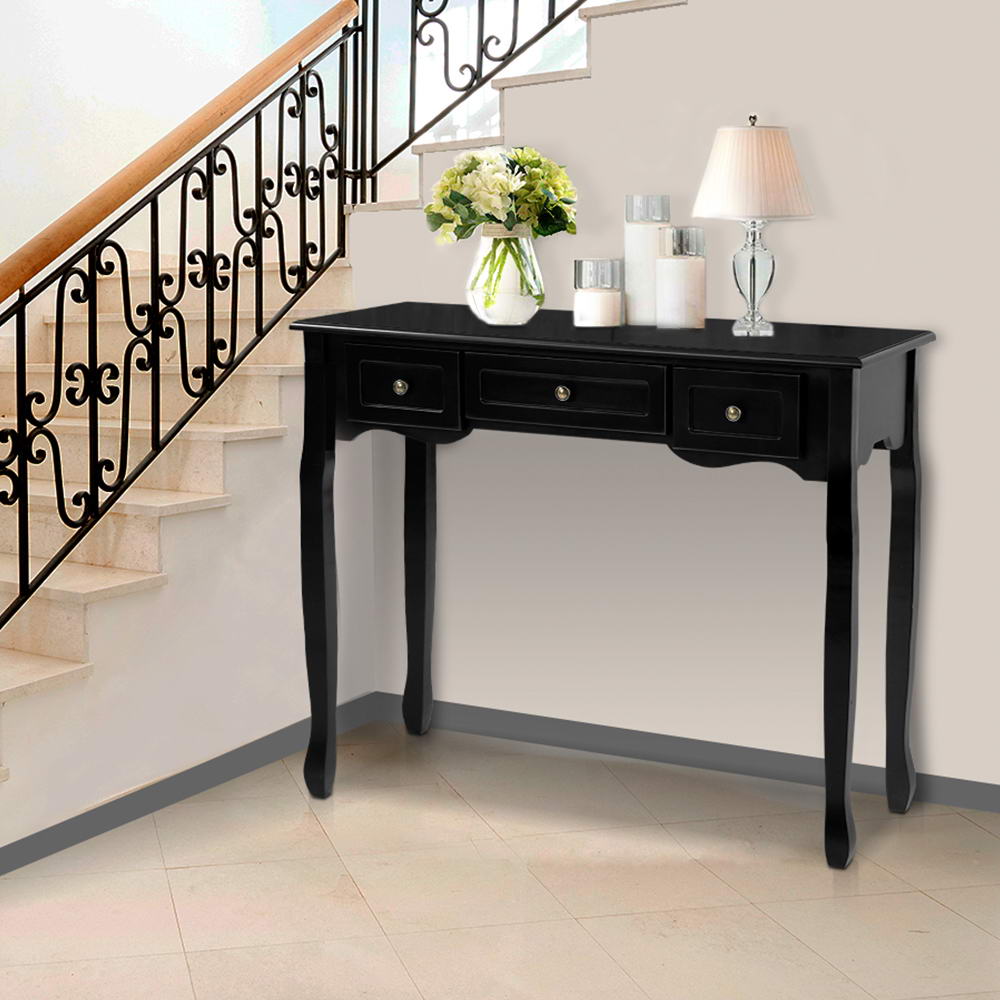 Black wooden console table with three drawers and ornate cabriole legs styled with flowers and lamp by staircase