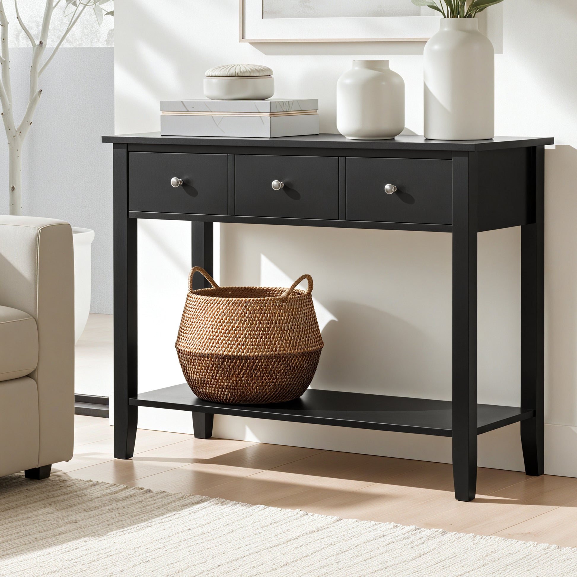 Black console table with three drawers and lower shelf in living room, styled with white vases and wicker basket