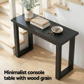 Black wood-grain console table in staircase hallway with books and keys, text 