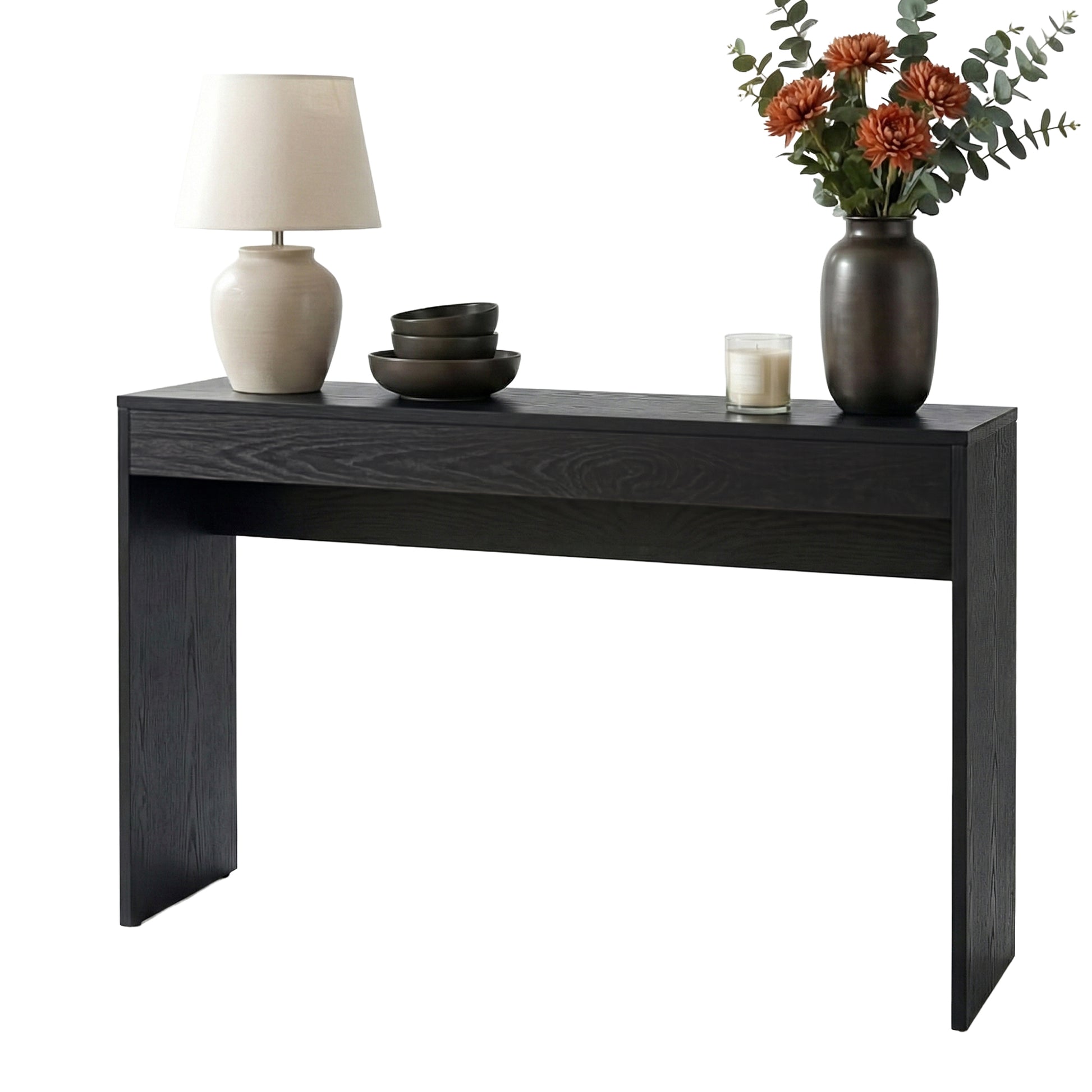 Black wood-grain console table styled with cream lamp, stacked dark bowls, candle and vase of orange flowers