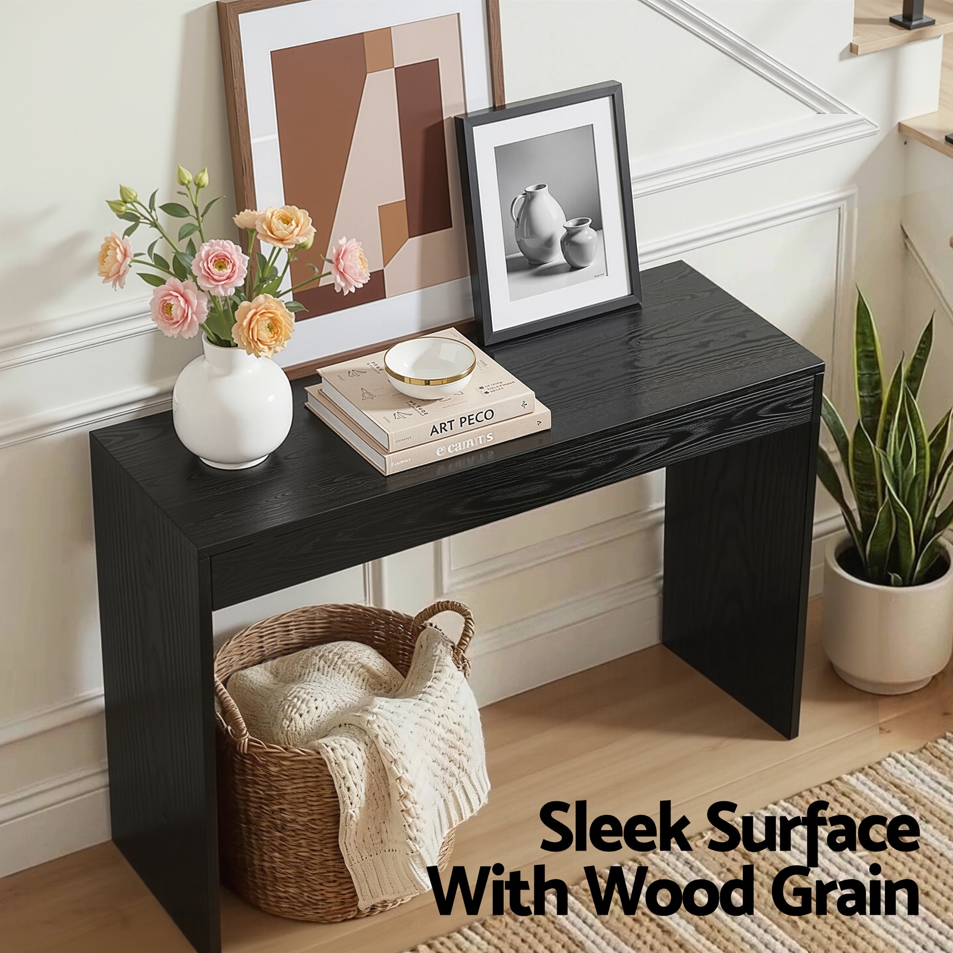 Black console table styled in entryway with text "Sleek Surface With Wood Grain", vase of roses, framed prints