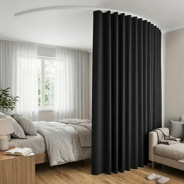 Black room divider curtain on white curved ceiling track in bedroom with grey bed sheer curtains plant and beige sofa