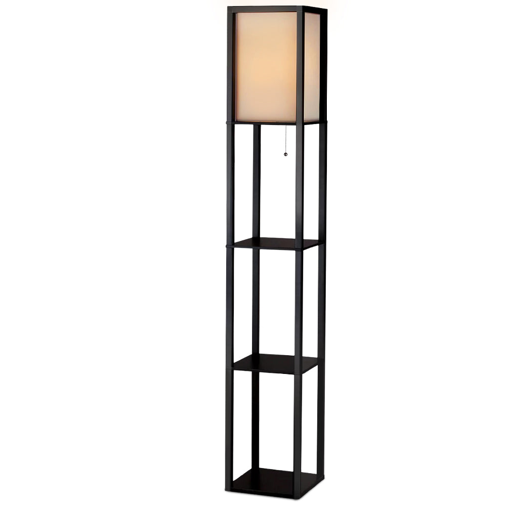 Black fabric shelf floor lamp in living room with leather sofa, three shelves holding decorative bottle and white vases
