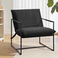 Black fabric sling armchair in room with sheer curtains and light wood floor, bookcase at left, large plant at right