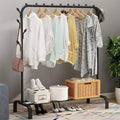 Black steel garment rack with bottom shelf loaded with hanging clothes bags shoes and basket in living room
